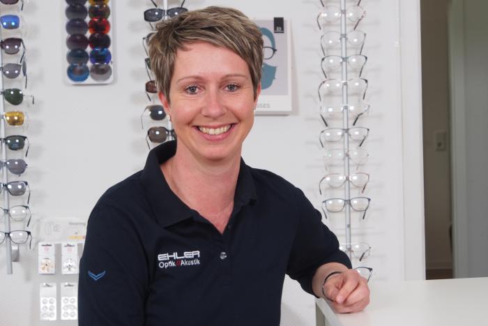 Simone Sievertsen steht im Fachgeschäft von Ehler Optik & Akustik und hält eine Brillenfassung in den Händen